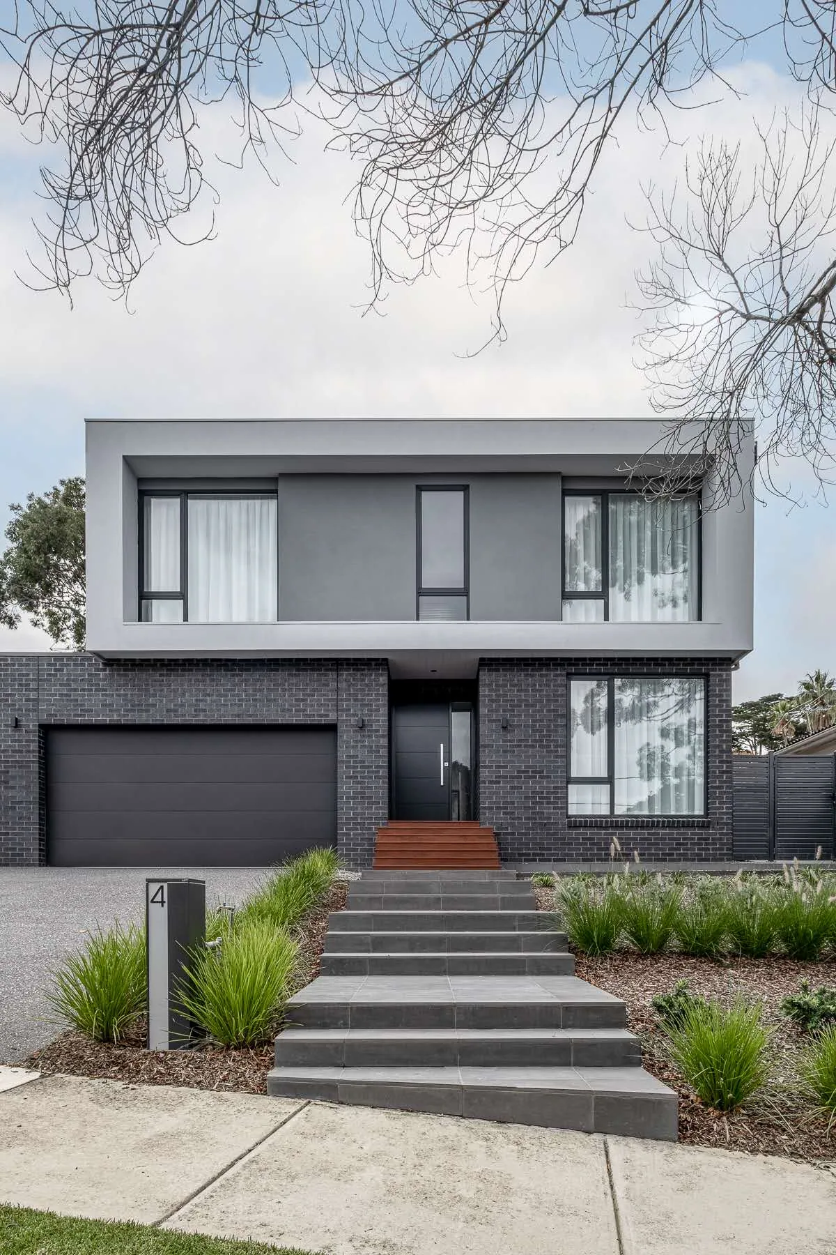 Box Hill Residence: A dark, framed street elevation opens into a light interior arranged around a generous double-height void.